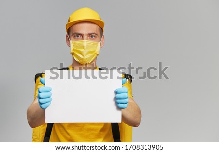 Courier in yellow uniform, protective mask and gloves Holding a white sign for text. Delivery service under quarantine. 