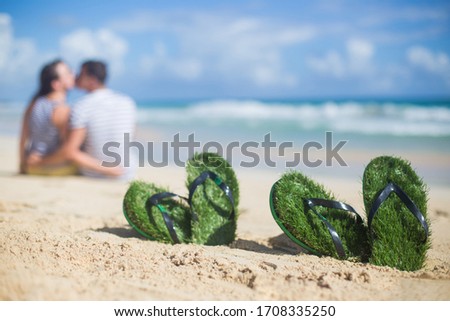Flip flops on the sandy beach with romantic couple kissing and hugging in front of the ocean and blue sky background on a sunny day