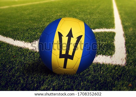 Barbados flag on ball at corner kick position, soccer field background. National football theme on green grass.