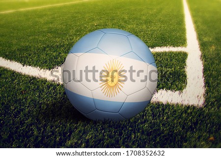 Argentina flag on ball at corner kick position, soccer field background. National football theme on green grass.