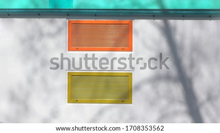 air outlet in the wall of the building with a cracked tree, iron grille of colored blinds, painted