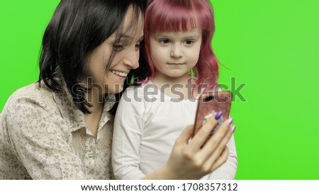 Cute funny little kid girl having fun with mom enjoy using modern gadget smart phone looking at mobile screen laughing making conference call in app, watching social media video. Chroma key