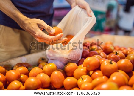 Man chooses tomatoes in a supermarket without using a plastic bag. Reusable bag for buying vegetables. Zero waste concept
