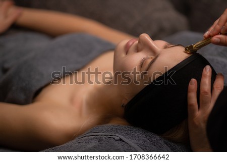 close-up photo of woman getting massage on forehead with the use of jade or mesotherapy roller by professional masseur or cosmetologist, woman enjoy procedure, lie with closed eyes