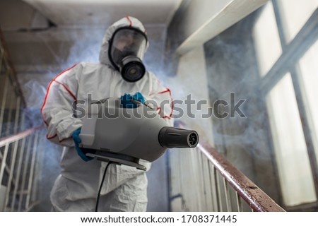 professional disinfector wearing protective biological suit and gas-mask conducts disinfection against coronavirus global pandemic warning and danger. COVID-19, coronavirus concept Royalty-Free Stock Photo #1708371445