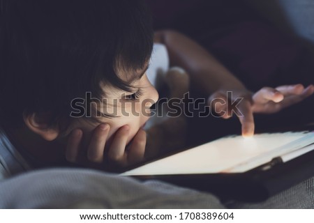 Low key light Kid touching screen on tablet searching information on internet, Child boy playing game or watching cartoon on digital tablet,Stay at home, Distance education or home schooling concept