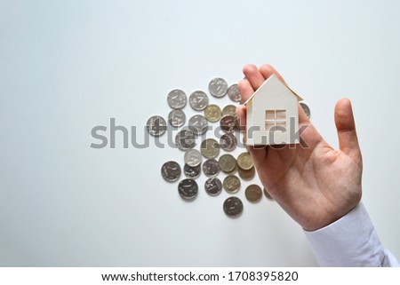 Paper house on the palm on the background of coins copy space. Mortgage loan concept.