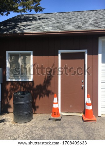 A brown door that is the entrance to a maintenance building with two orange cones. 