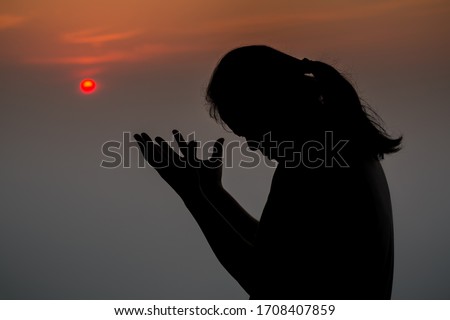 Silhouette of woman praying in the morning over beautiful sunrise background