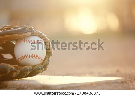 Baseball in glove on ball field during sunset at park, copy space on blurred background with shallow depth of field. Sports concept for game or athlete.