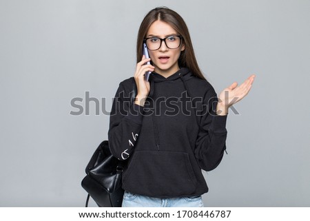 Attractive stylish girl laughing cheerfully while talking on mobile phone to her boyfriend, isolated on gray background. Conversation concept. Happy hipster teacher wearing glasses with coffee