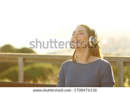 happy confident girl enjoying listening music on headphones at sunset on a park