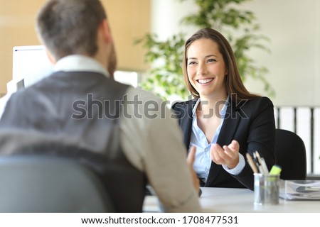 Happy executive coworkers laughing and talking sitting on a desk at the office Royalty-Free Stock Photo #1708477531
