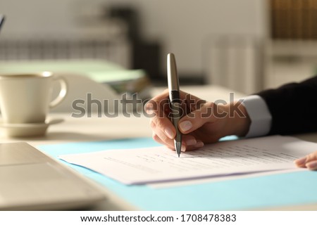 Close up of business woman hands filling out form at night in the office