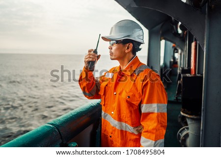Filipino deck Officer on deck of vessel or ship , wearing PPE personal protective equipment. He holds VHF walkie-talkie radio in hands. Dream work at sea Royalty-Free Stock Photo #1708495804