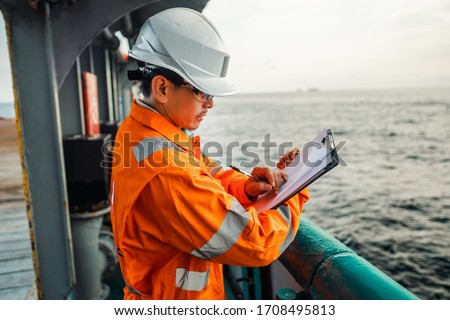 Filipino deck Officer on deck of offshore vessel or ship , wearing PPE personal protective equipment. He fills checklist. Paperwork at sea Royalty-Free Stock Photo #1708495813