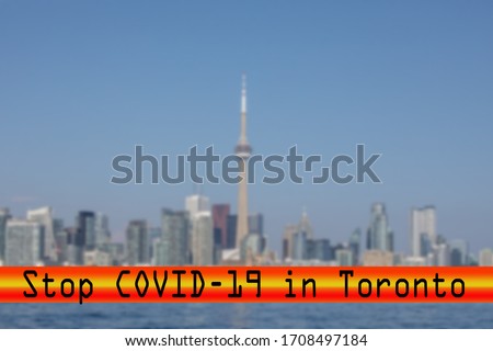 a futuristic font stop covid-19 red banner over a blurred skyline of Toronto