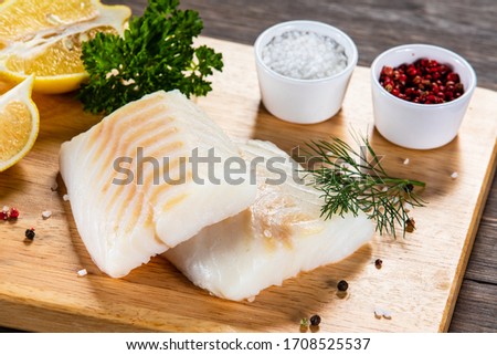 Fresh raw cod with seasonings and vegetables served on cutting board on wooden table 