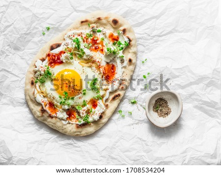Delicious breakfast - flatbread with fried egg, greek yogurt, chili sauce and cheese on light background, top view       
