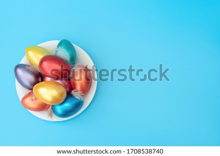Decorated Easter eggs with small feathers lie on the plate on blue background. Happy Easter holiday concept. Greeting, invitation card. Flat lay style with copy space.