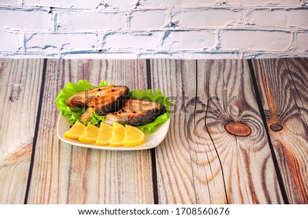 Two steaks of pink salmon fillet on a plate decorated with lettuce and slices of lemon are on a wooden table. Flat lay.
