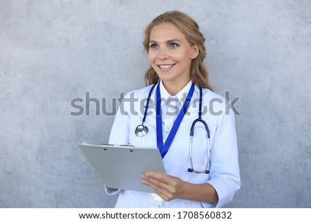 Smiling female doctor with stethoscope holding health card isolated over grey background.
