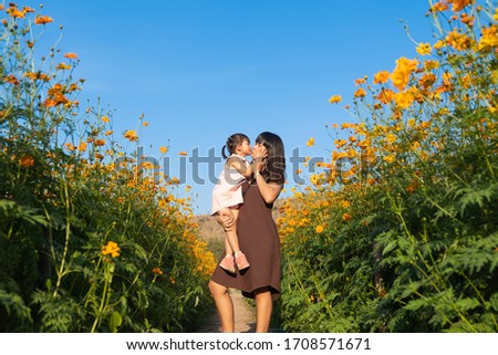 Asian mother and daughter kiss in the flower field, on nature background.