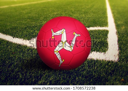 Isle Of Man flag on ball at corner kick position, soccer field background. National football theme on green grass.
