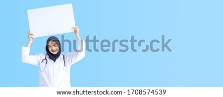 Young Arab Muslim doctor women smile showing white card on wide blue background concept for Islam people working in medical hospital health care, Nurse wear hijab in pandemic stay home panoramic text.