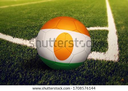 Niger flag on ball at corner kick position, soccer field background. National football theme on green grass.