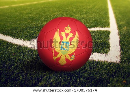 Montenegro flag on ball at corner kick position, soccer field background. National football theme on green grass.