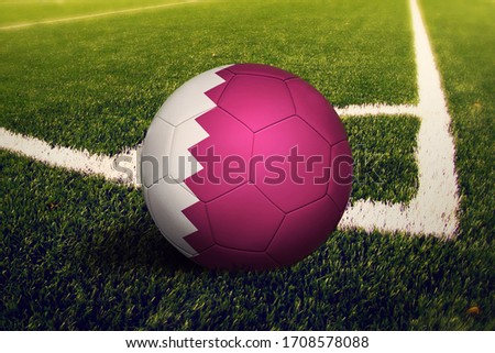 Qatar flag on ball at corner kick position, soccer field background. National football theme on green grass.