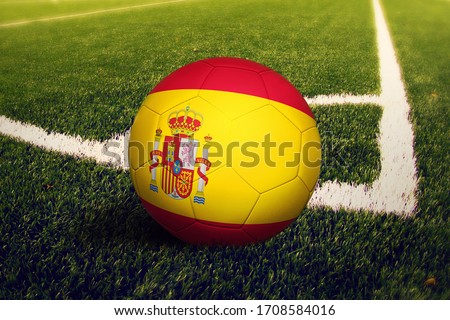 Spain flag on ball at corner kick position, soccer field background. National football theme on green grass.