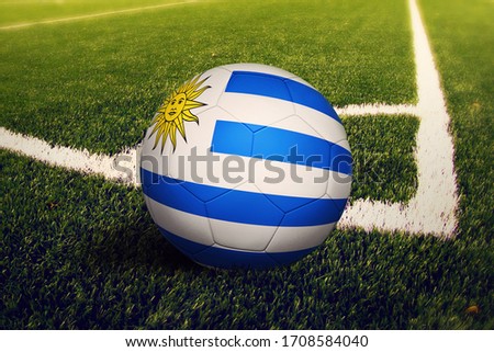 Uruguay flag on ball at corner kick position, soccer field background. National football theme on green grass.