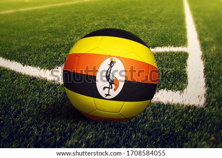 Uganda flag on ball at corner kick position, soccer field background. National football theme on green grass.