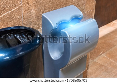 Modern vertical hand dryer with ultraviolet radiation and bin for used paper towels in public restroom WC
