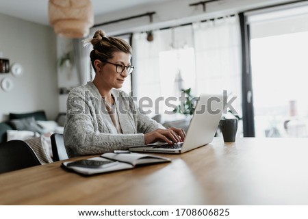 Businesswoman working on laptop computer sitting at home and managing her business via home office during Coronavirus or Covid-19 quarantine Royalty-Free Stock Photo #1708606825