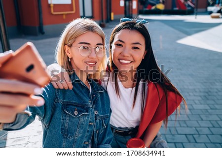 Portrait of happy friends smiling at front smartphone camera for making selfie influence content, cheerful hipster girls resting at urban setting using cellular technology for clicking photo pictures