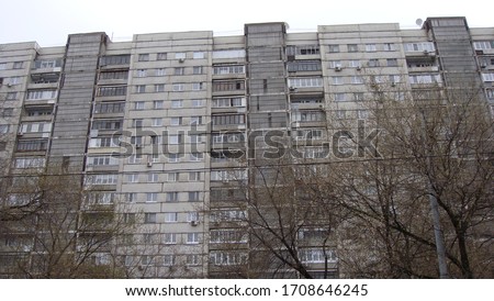 Old gray high-rise apartment building and trees in front of it