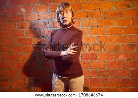 A middle-aged woman poses showing clothes near red brick wall. An inept model in non-professional shooting. Photography for sales turtleneck on the Internet or online store