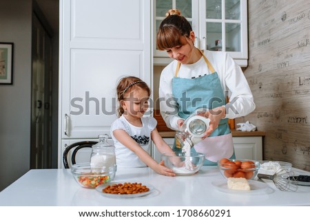 A girl helps her mother prepare a cake in the kitchen