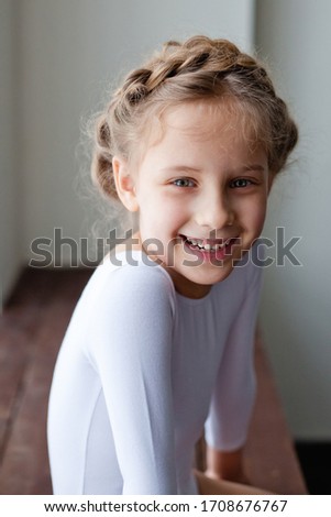 Large portrait of a little girl. Looking at the camera, she is genuinely, happily giggles-smiles. On a gray background.