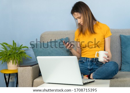 Young freelance female sitting on floor at home, working on laptop in home office