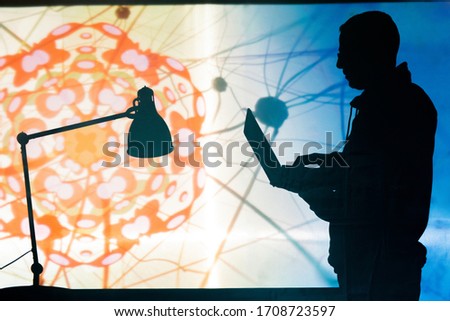 Silhouette of scientific engineer creating 3D model of coronavirus cell on laptop against bright projection screen Royalty-Free Stock Photo #1708723597