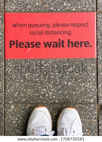 Sign on the floor outside a supermarket asking shoppers to “Please wait here” as part of social distancing measures to control the outbreak of Coronavirus in the UK