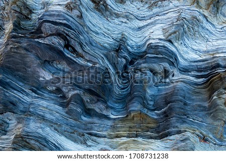 Marks of sea water and wind erosion on a blue toned rock from light to dark.The natural process of erosion created smooth and fluid lines, holes and sharp layers. carved. uneven surface stone. Nature Royalty-Free Stock Photo #1708731238