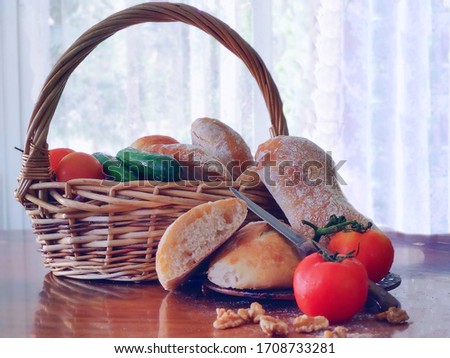 ciabatta sliced lies on a wooden table, tomato cucumber in a wicker basket