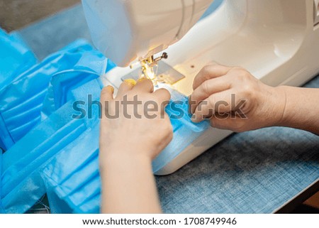 Sewing Homemade protective medical mask in process. woman holds a scanboard mask at home. Detail White modern sewing machine and three-layer masks. Selective Focus