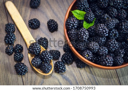 Ripe blackberries with leaves in a clay bowl on a light wooden background. Flat lay, top view. Photo of blackberry in clay bowl on wooden table. High resolution product. Royalty-Free Stock Photo #1708750993