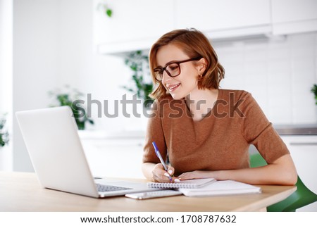 Woman on remote work or online education, using laptop computer, making  notes, indoors at office or home at daytime. Online business, young professional at workplace. Working from home. Royalty-Free Stock Photo #1708787632